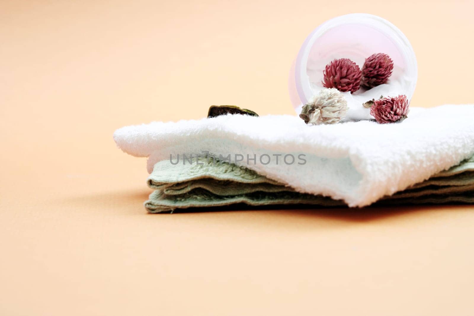Spa essentials (cream, white towel and pink flowers) isolated on yellow