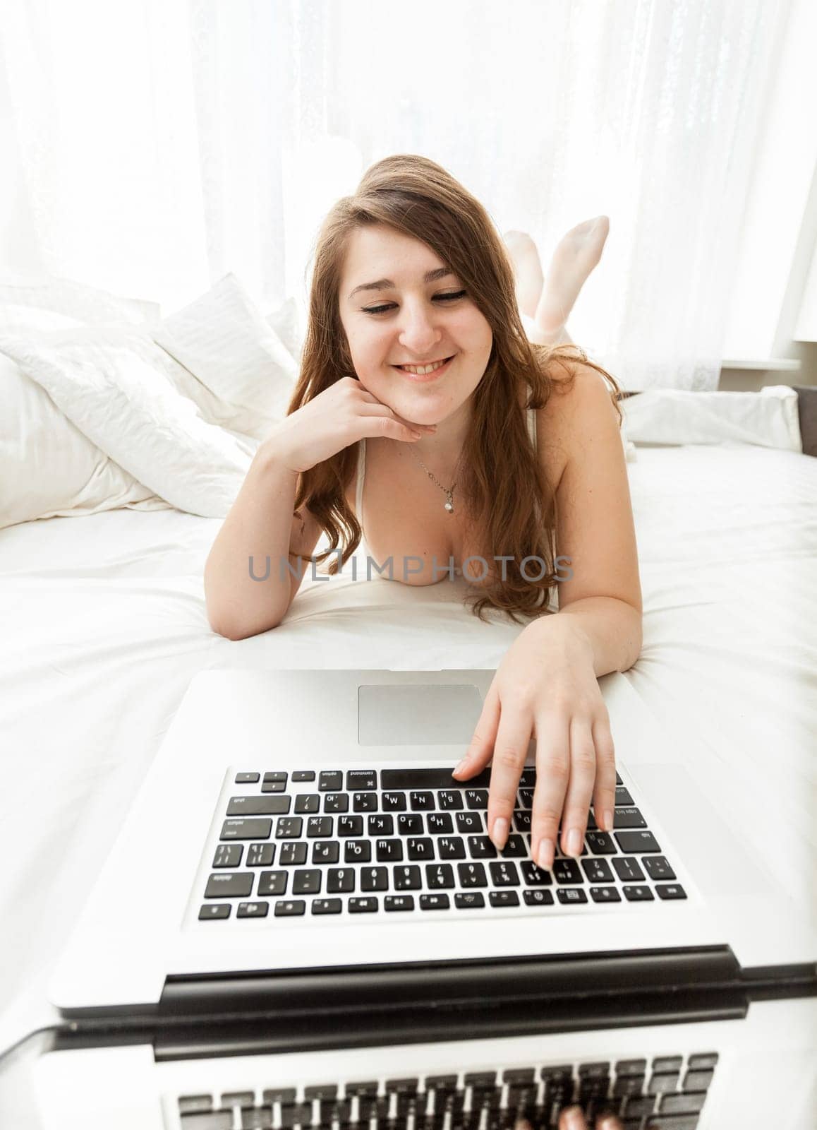 Closeup portrait of sexy woman typing on laptop keyboard in bed