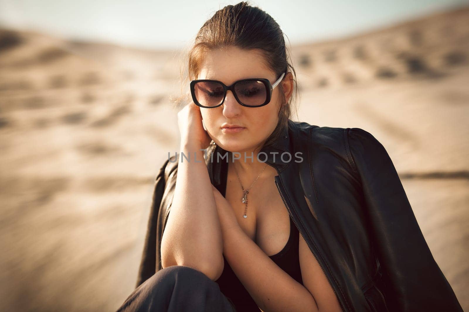 Closeup portrait of sexy woman in sunglasses sitting on sand dune