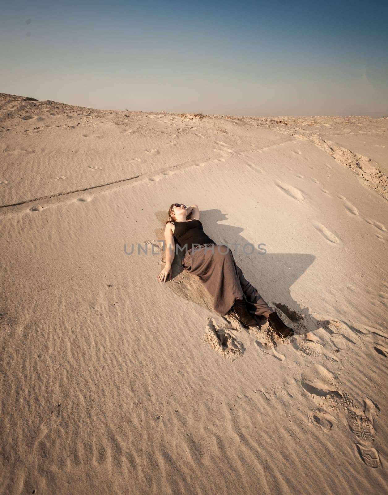 Beautiful woman in dress lying on sand dune at desert