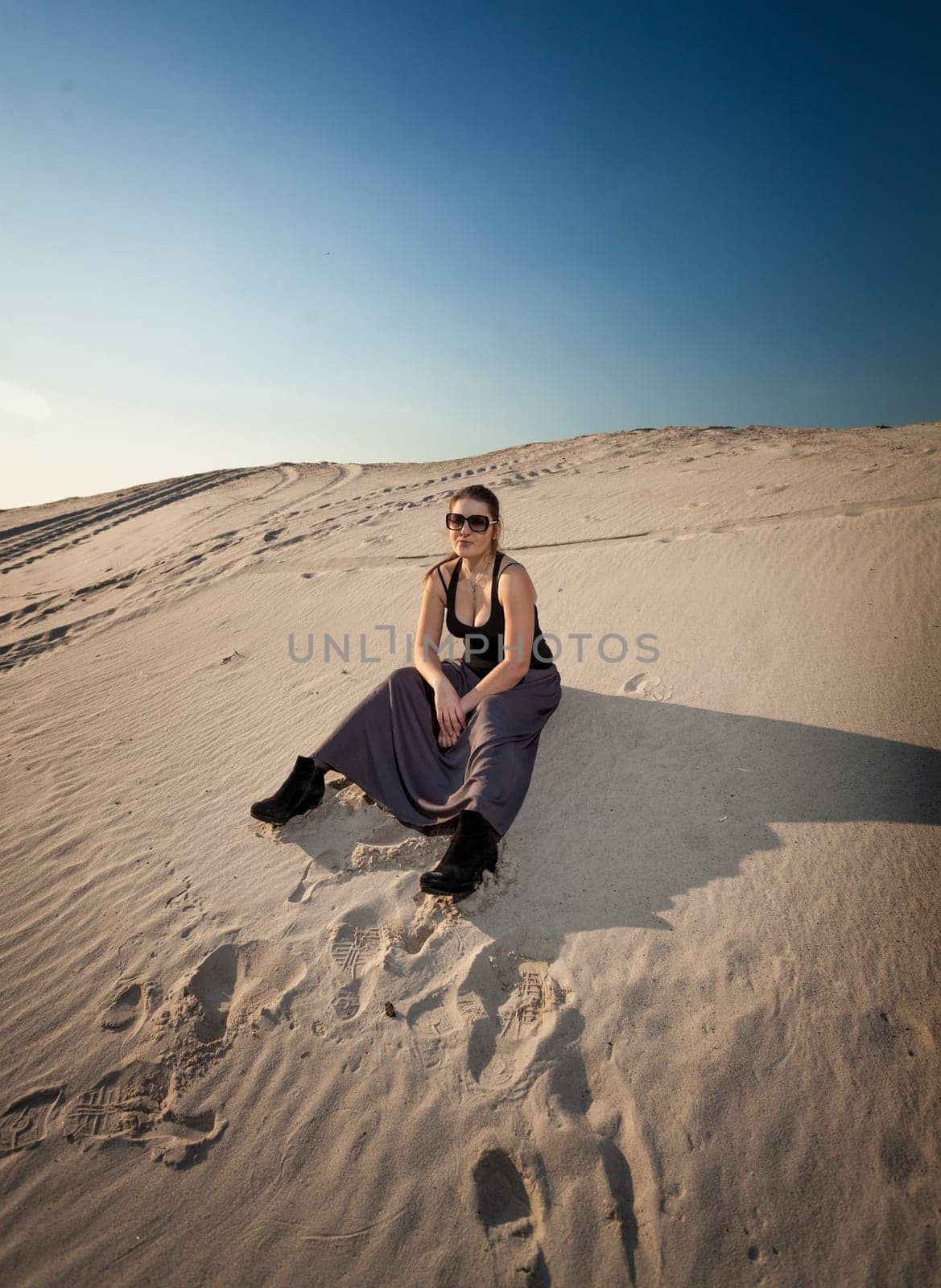 Beautiful woman in dress sitting on sand dune