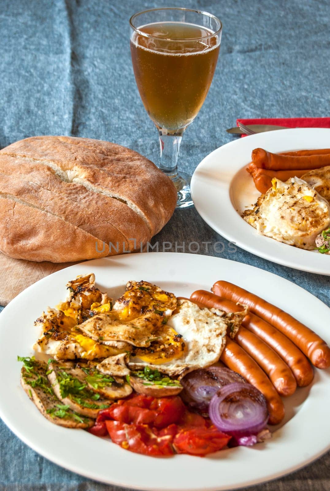 Table set with fried eggs, sausages, mushrooms, onions, tomatoes, bread and glass of beer