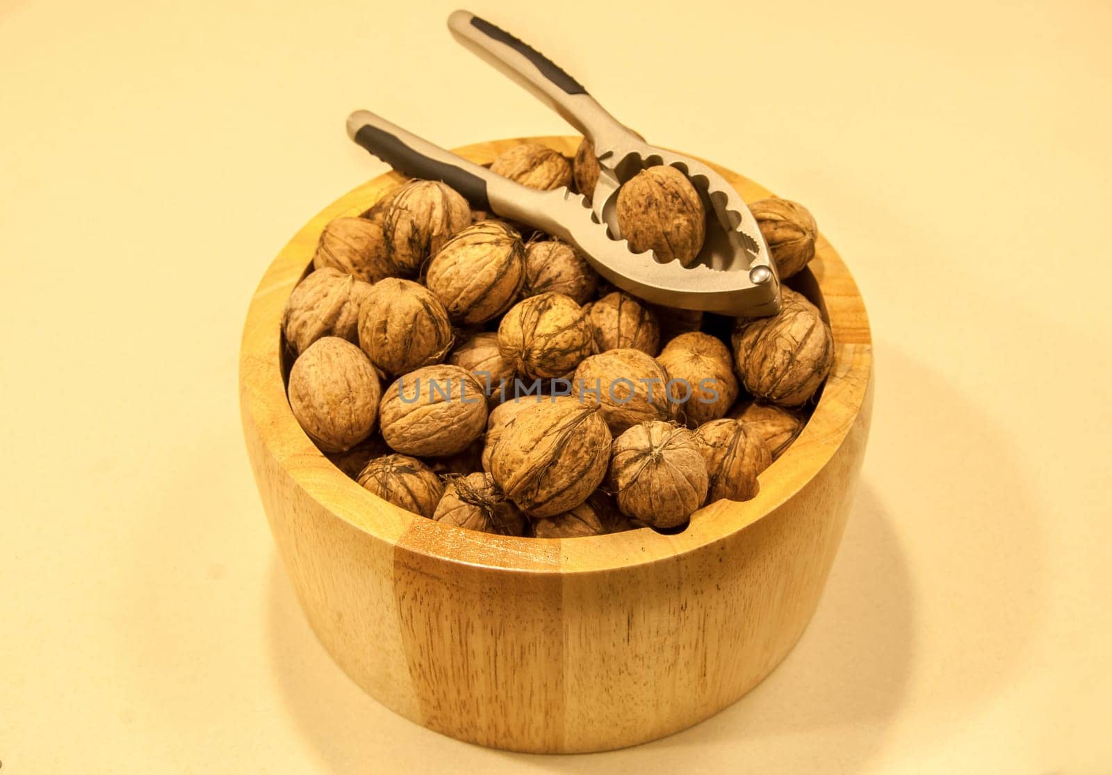 Wooden bowl with walnuts and nutcracker on a light background