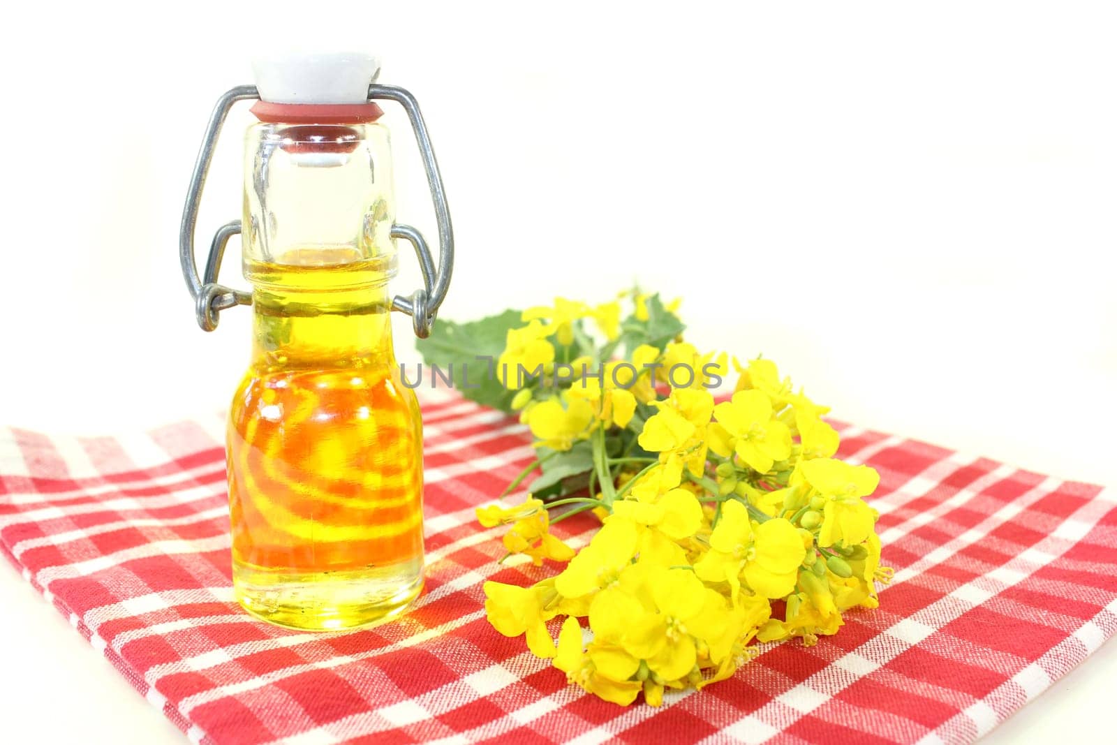 a bottle of rapeseed oil and rapeseed flowers against a white background