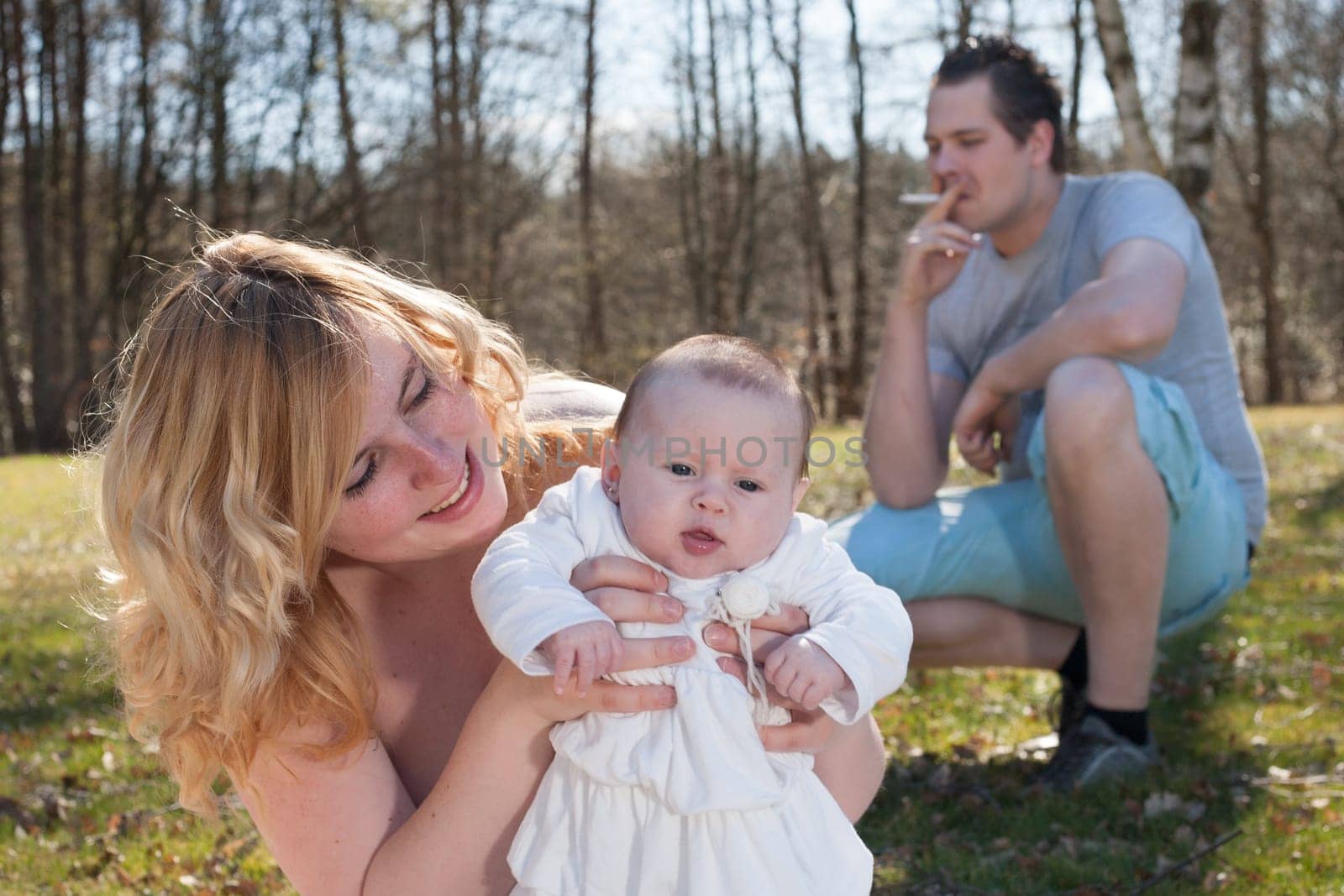 Young father is smoking while its unhealthy for his family. Distance between father and family