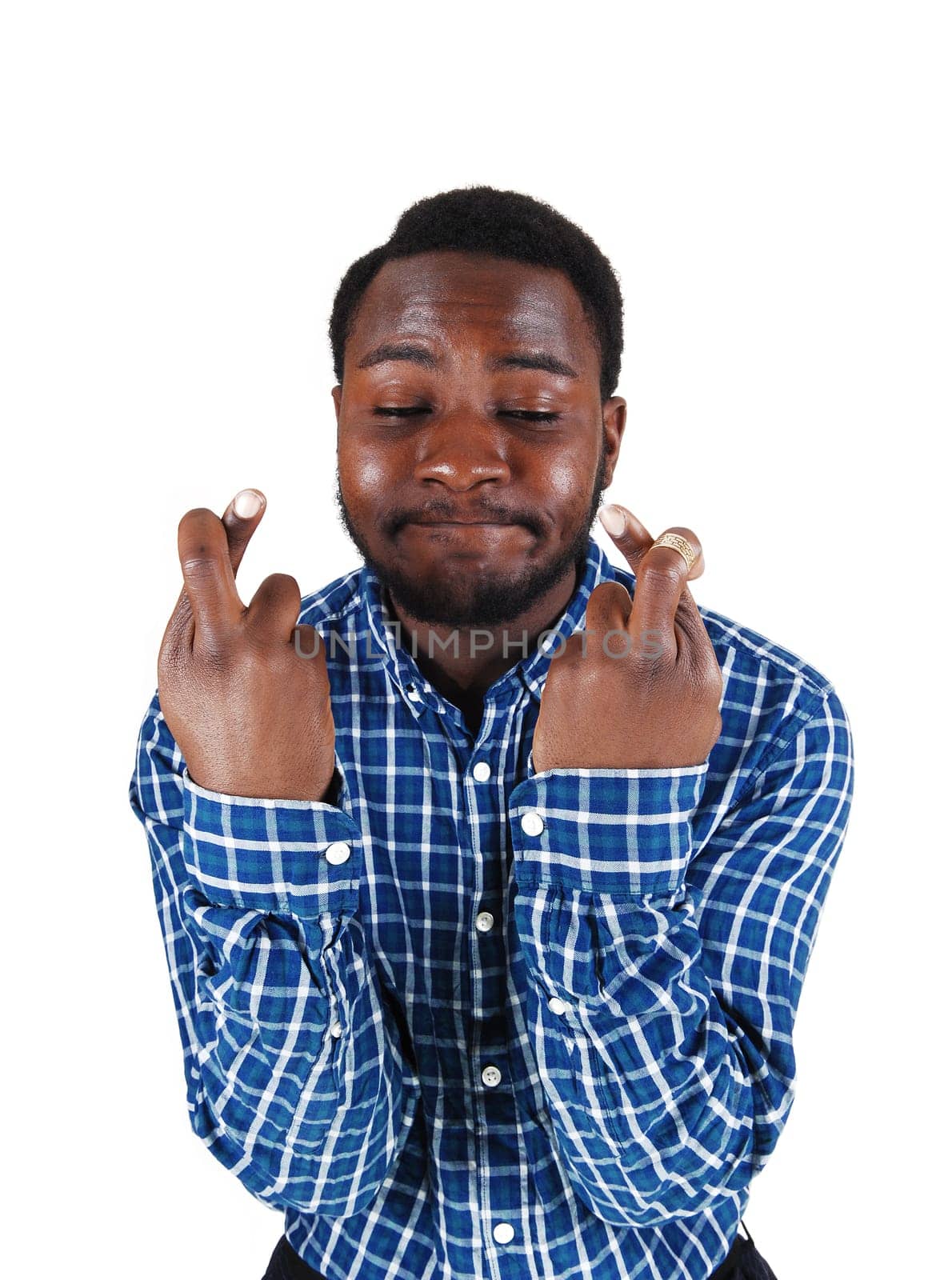A handsome young black man in a blue shirt with his arms up and.fingers crossed, isolated for white background..