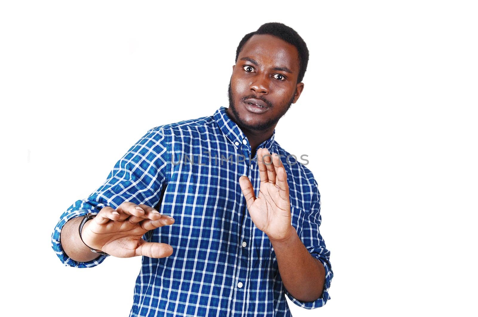 A scared looking young black man in a blue shirt with his arm's raised.standing isolated for white background..