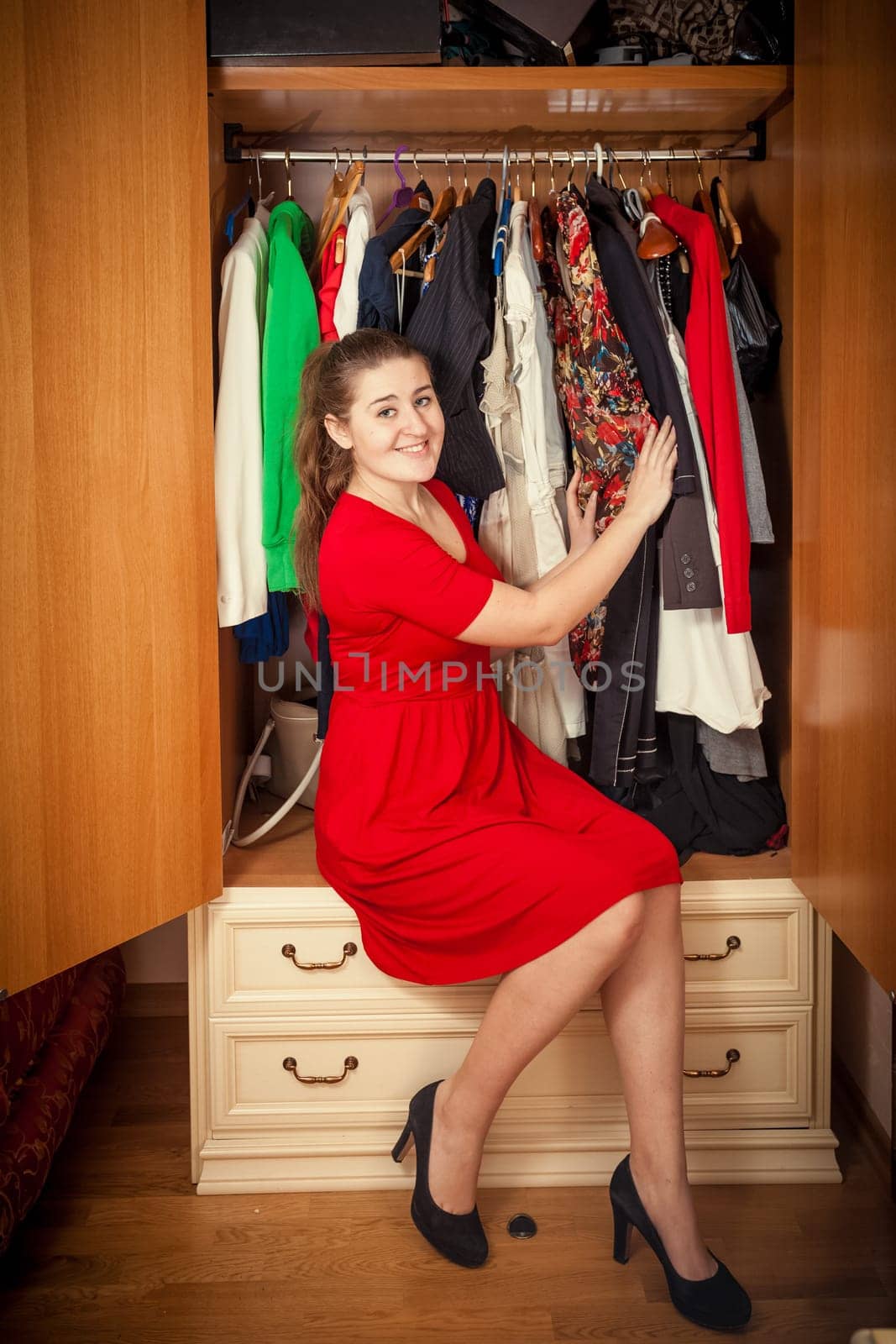 Photo of beautiful woman in red dress sitting at big wardrobe