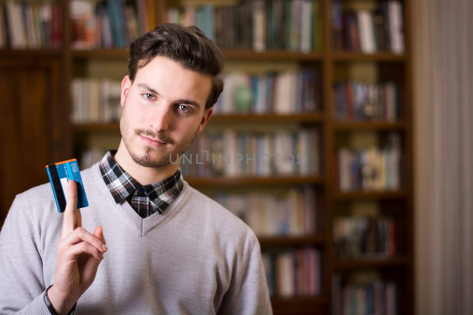 Attractive young man at home holding credit card, looking at camera