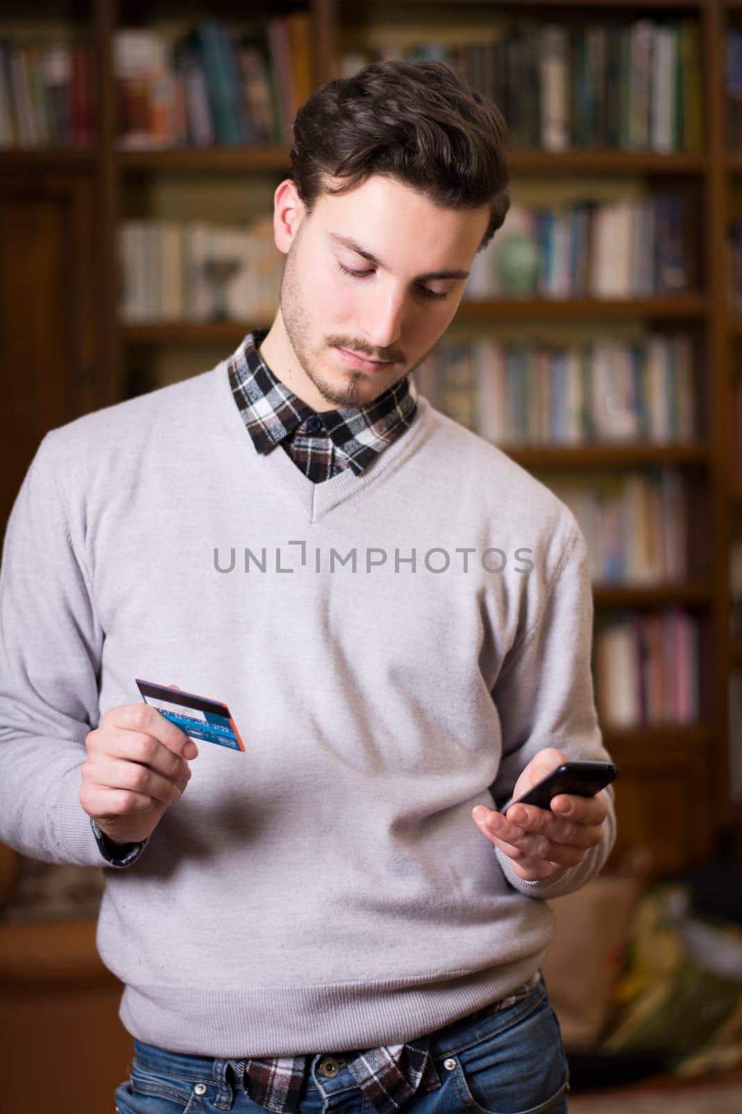 Attractive young man shopping online on mobile phone, holding credit card
