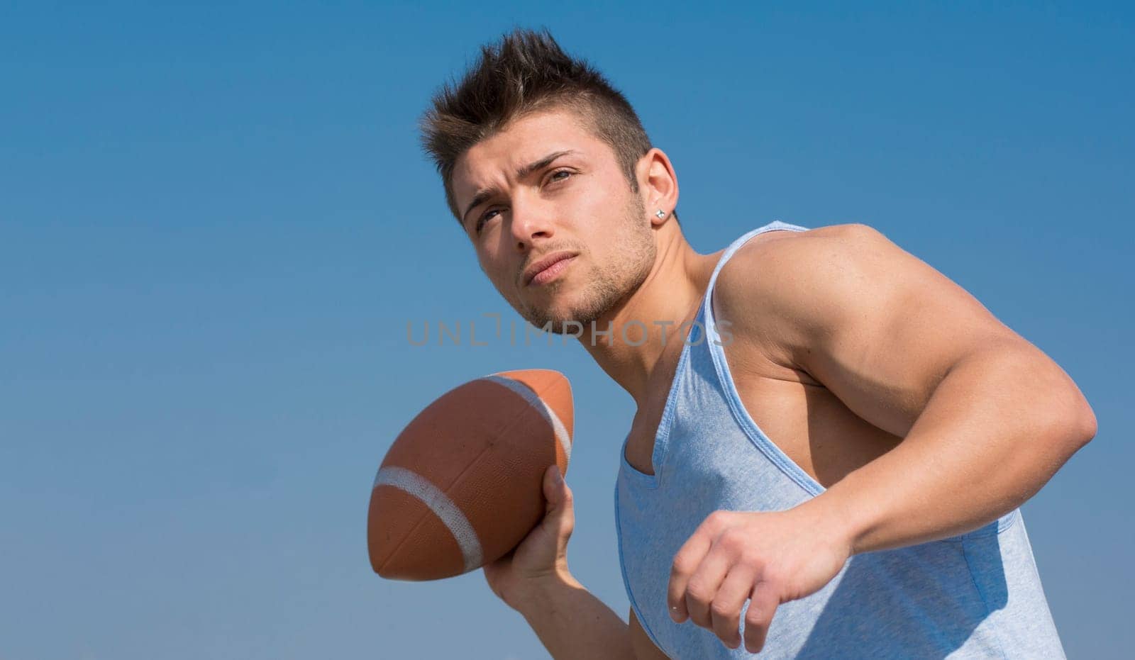 Muscular american football player ready to throw ball in hand. Outdoors shot