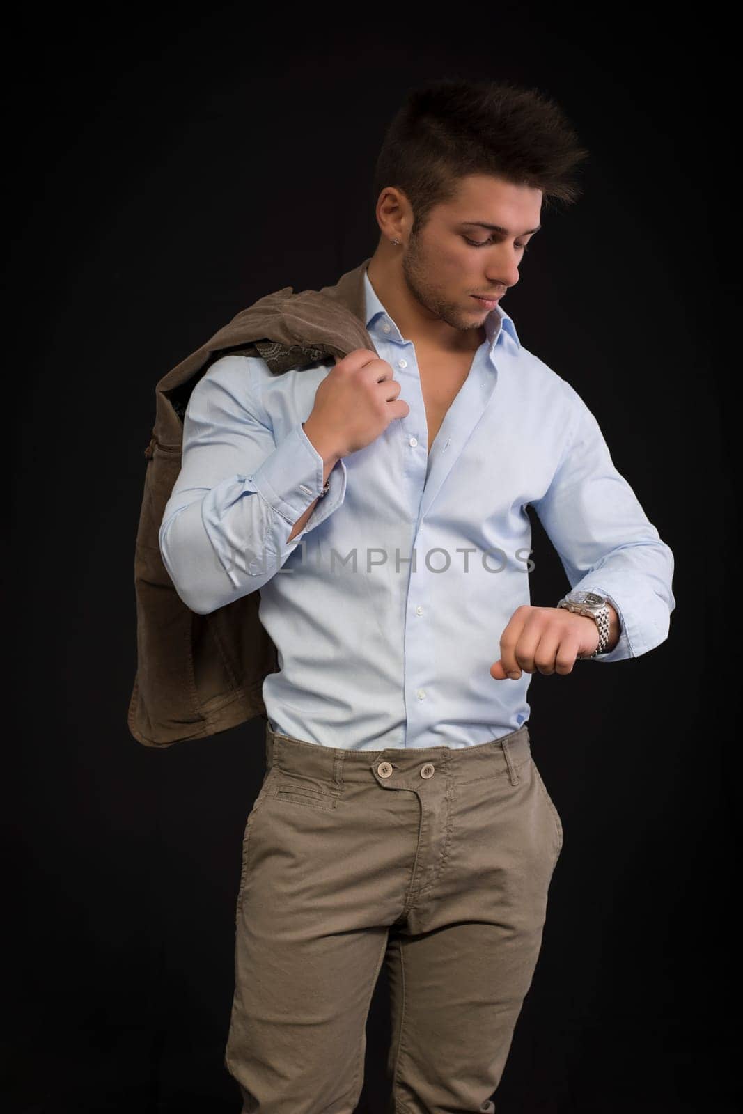 Handsome young man checking watch on his wrist, isolated on black