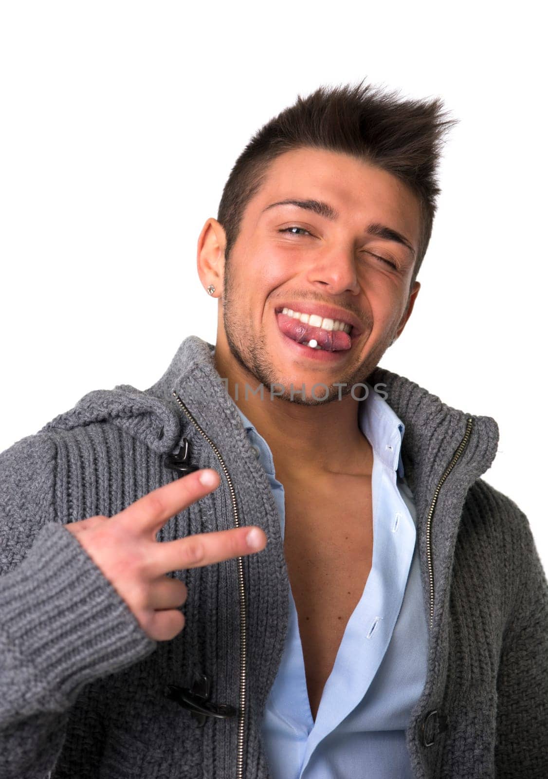 Attractive young man smiling with tongue piercing, doing victory sign with two fingers