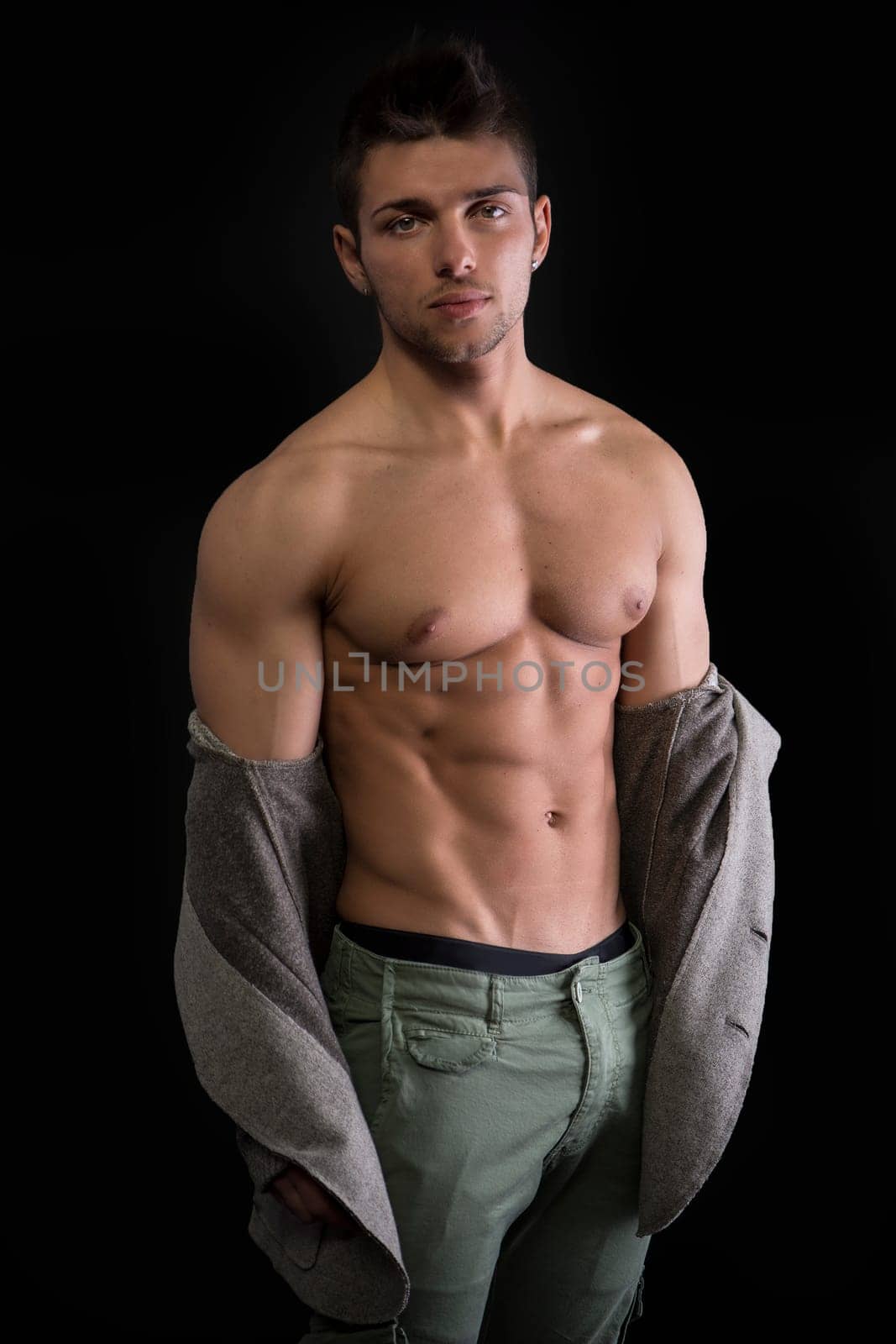 Confident, attractive young man with open jacket on muscular torso, ripped abs and pecs. Side view