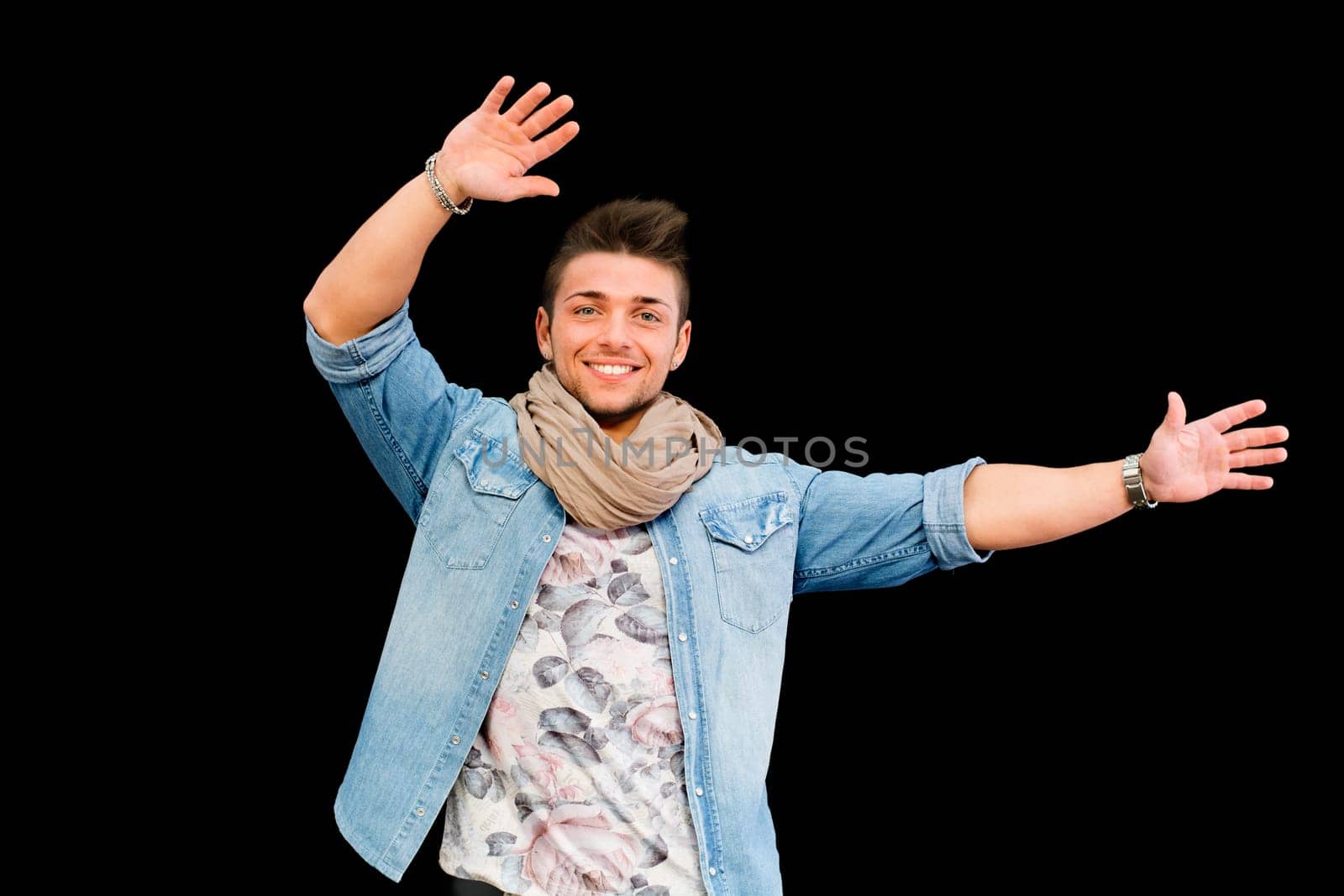 Cheerful young man dancing, moving arms up in the air, isolated on black background