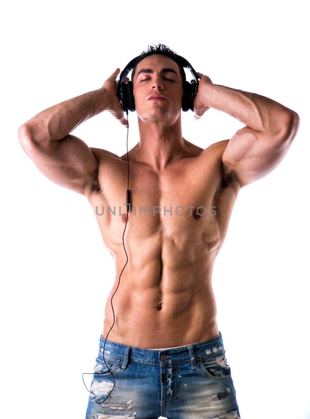 Muscular man shirtless, standing, listening to music on headphones, with eyes closed