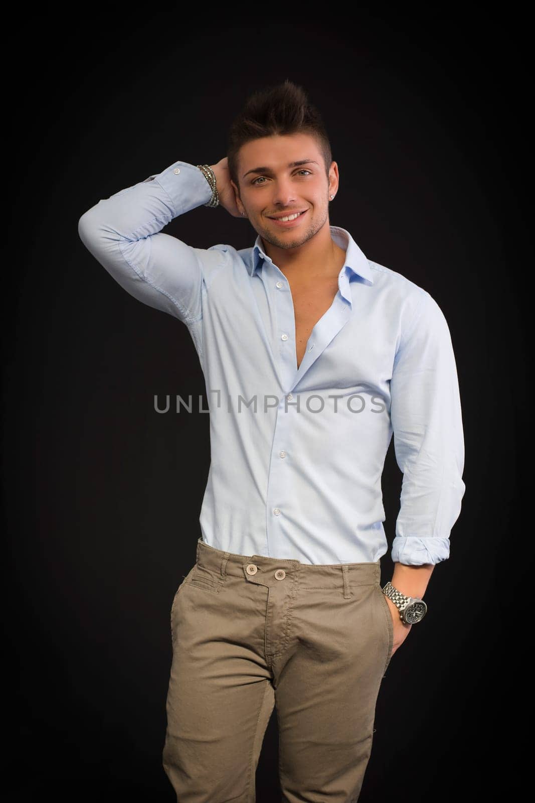 Handsome young man portrait, smiling and standing on dark background, hand in pocket