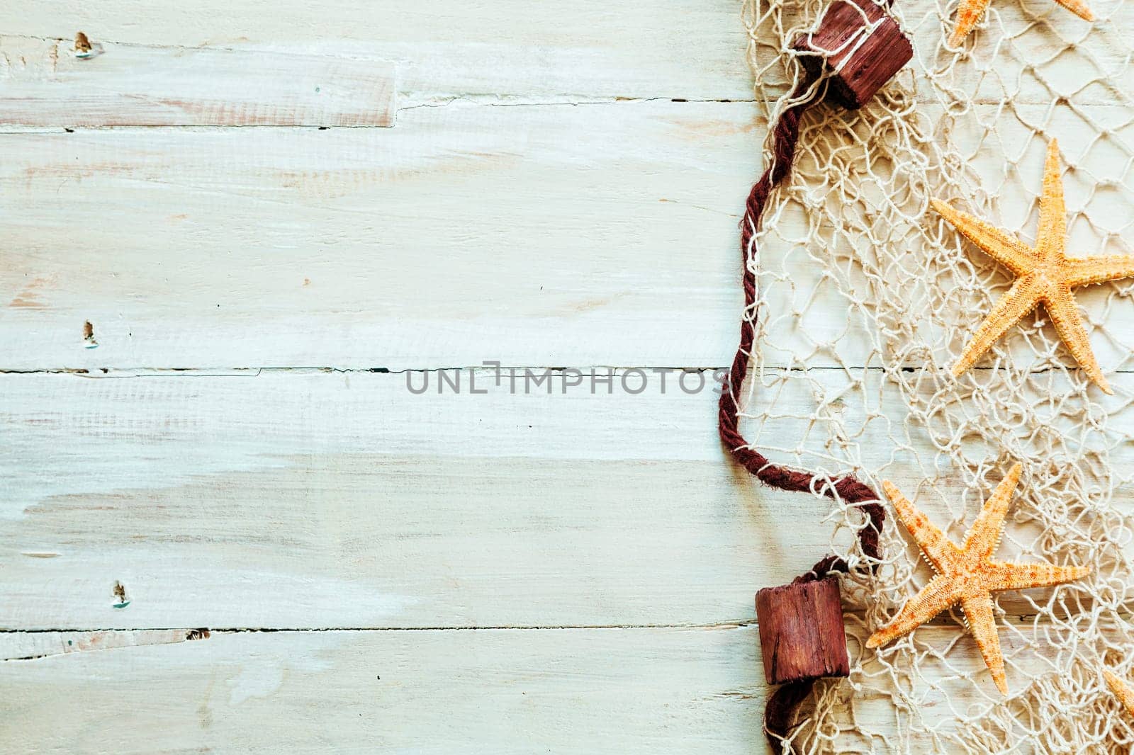 Nautical border formed of fishing net edged with corks entangled with scattered starfish on light beige wooden boards with copyspace for your text or advertisement
