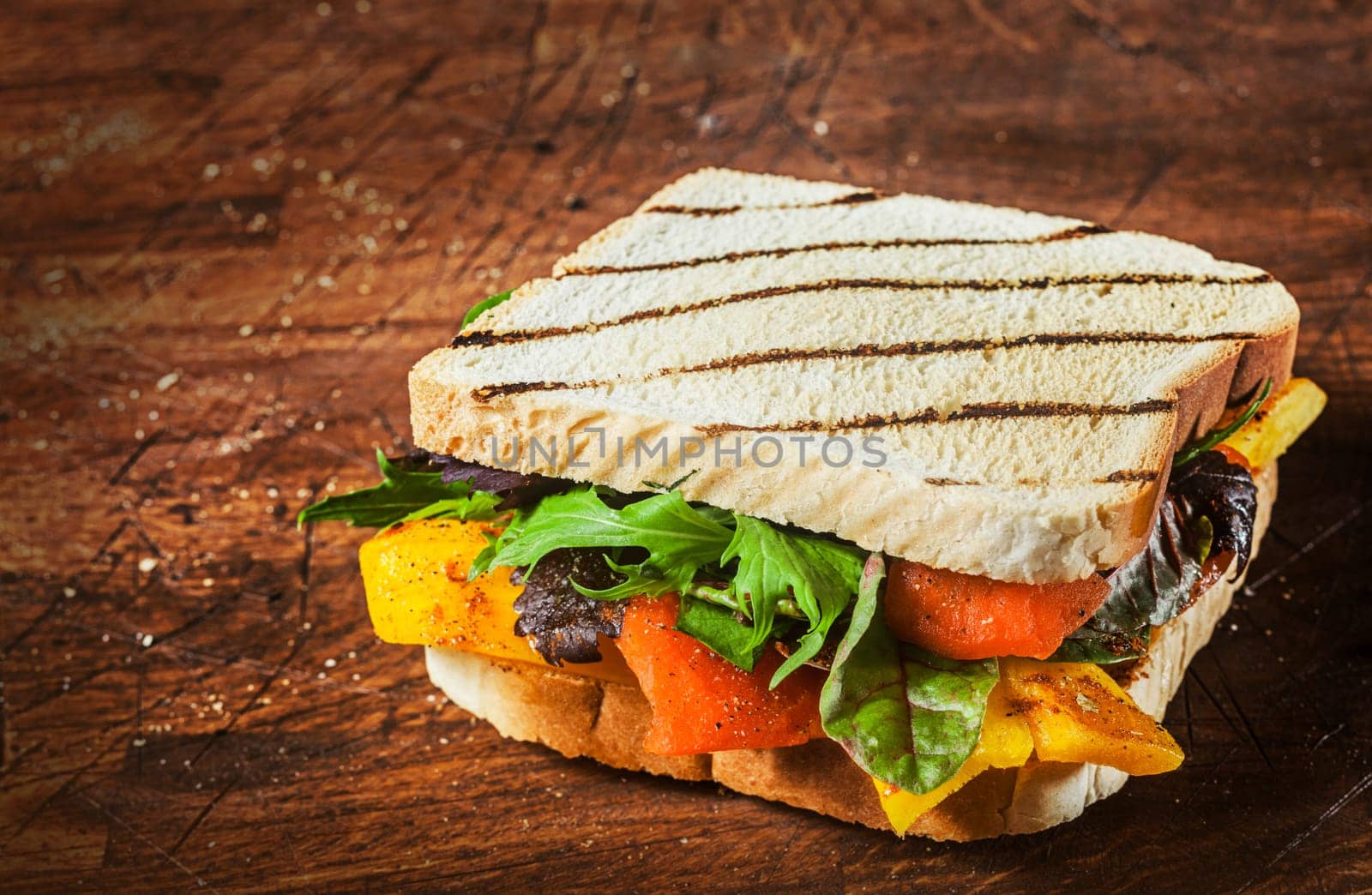 Grilled wholewheat cheese and salad sandwich with pepper, spinach and rocket served on a rustic wooden counter with copyspace