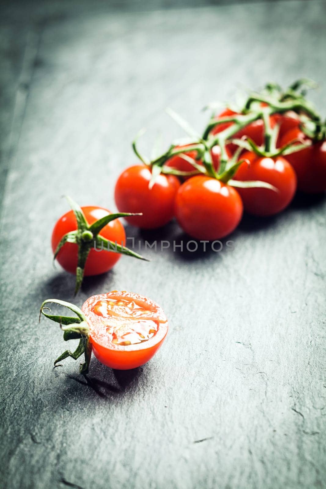 Grape tomatoes on the vine with a single halved tomato in the foreground on a textured surface with highlight and copyspace and shallow dof