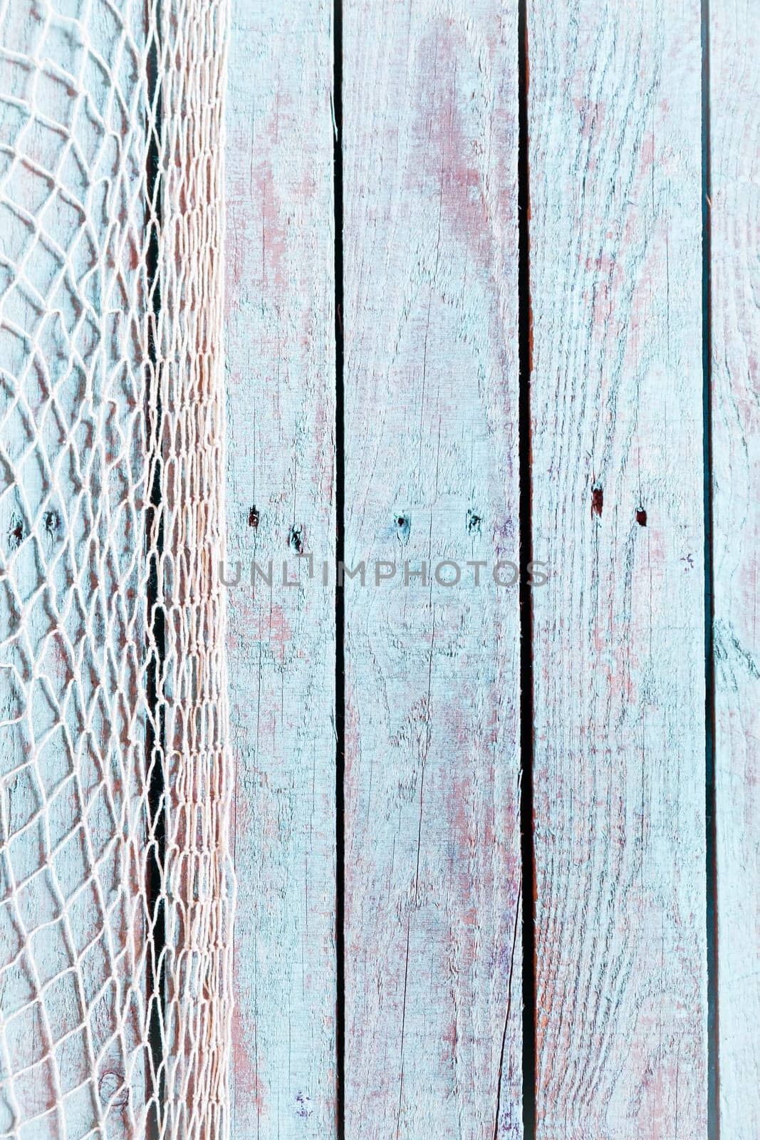 Fishing net former a vertical border on the left of old rustic blue painted weathered wooden boards with copyspace in a marine background