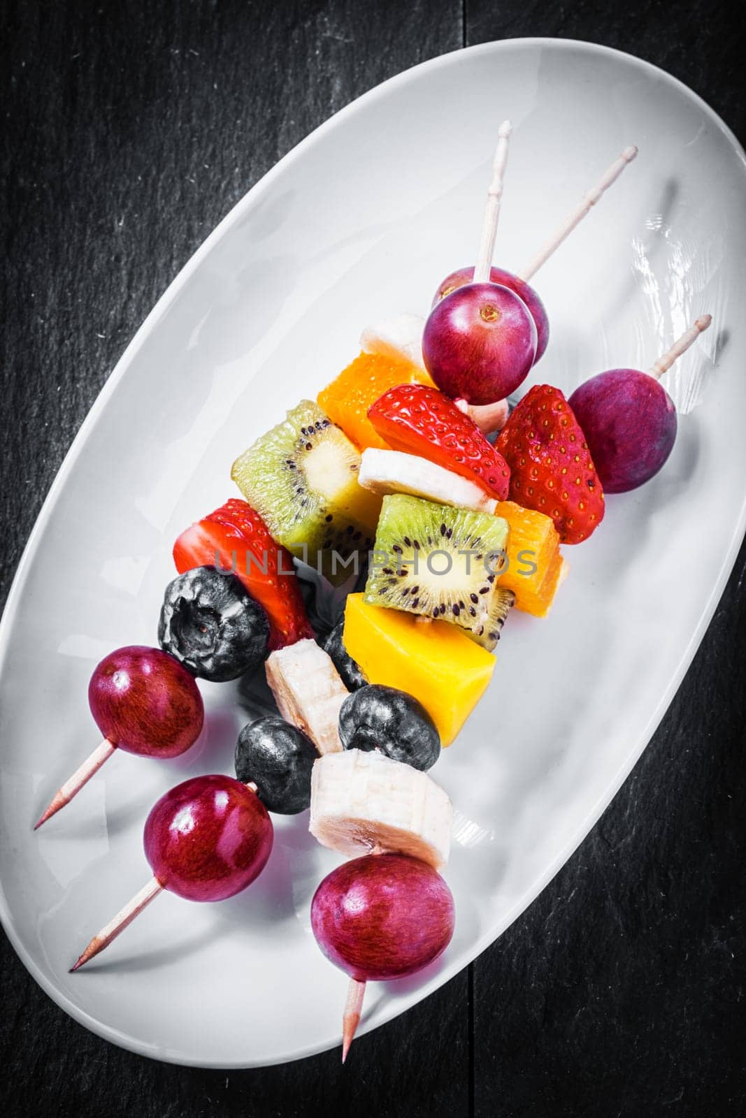 Close up overhead view of delicious healthy fruit kebabs with strawberries, blueberries and tropical fruit including kiwifruit, orange and banana