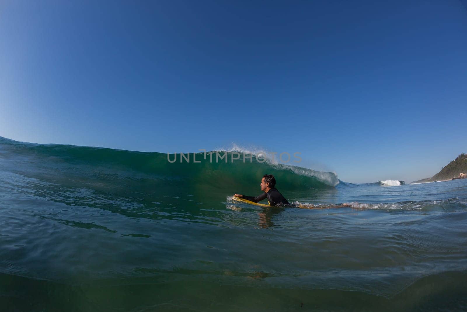 Ocean wave crashing on shallow reef with body-boarder paddling out to catch next surfing wave.