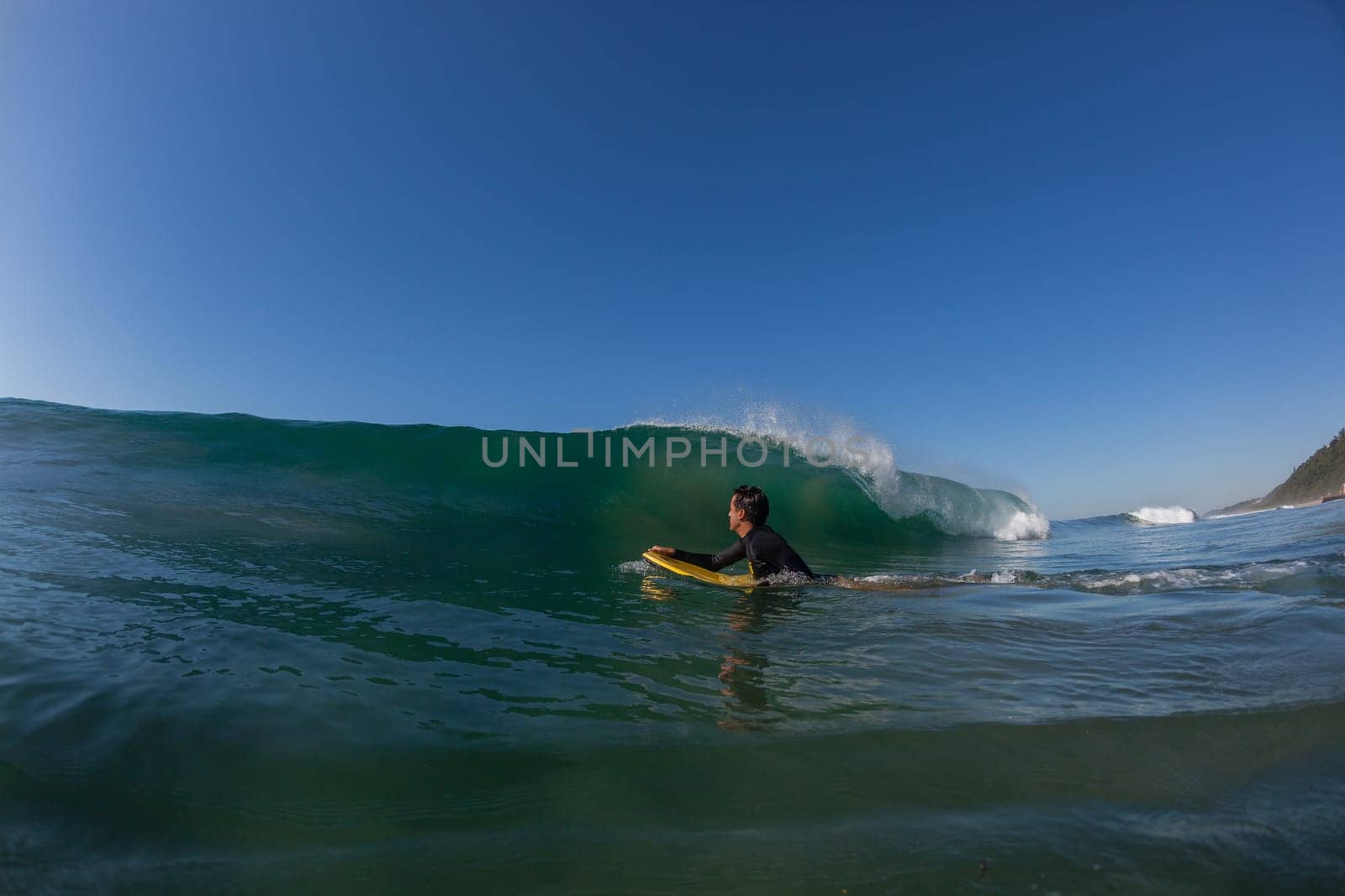Ocean wave crashing on shallow reef with body-boarder paddling out to catch next surfing wave.