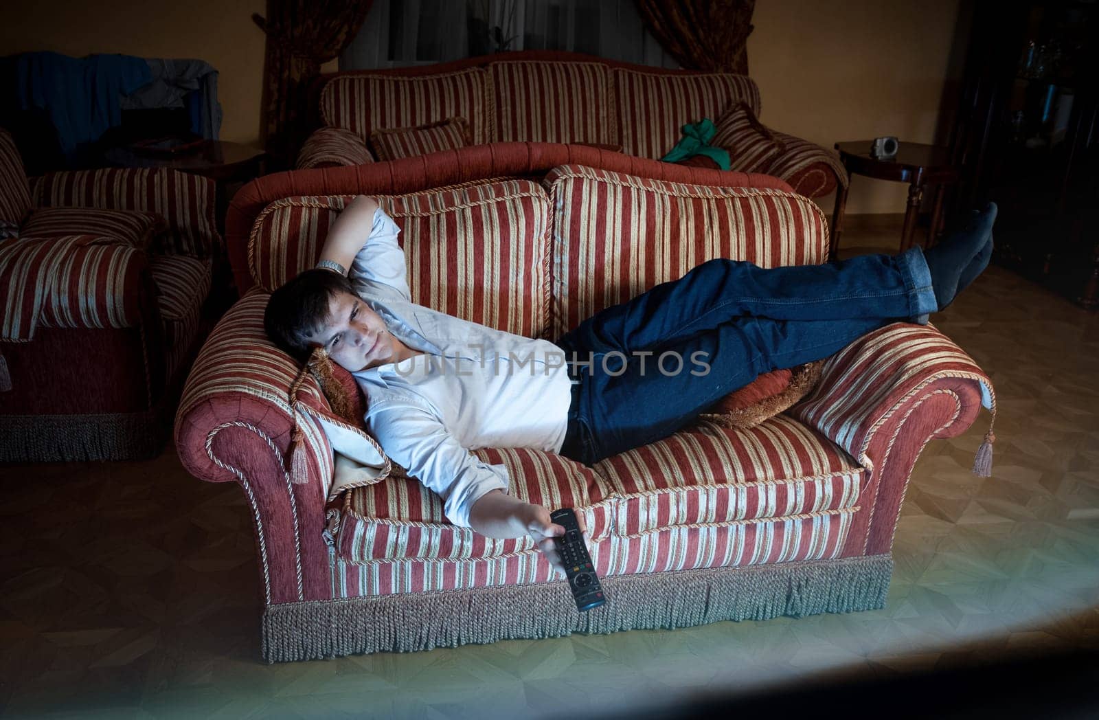 Portrait of man switching TV channels on sofa at night