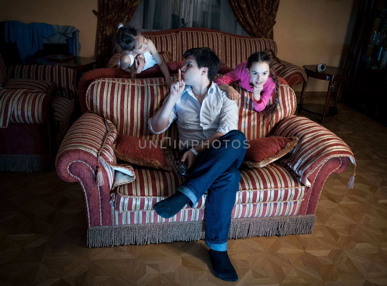 Photo of two daughters disturbing father while watching TV at night