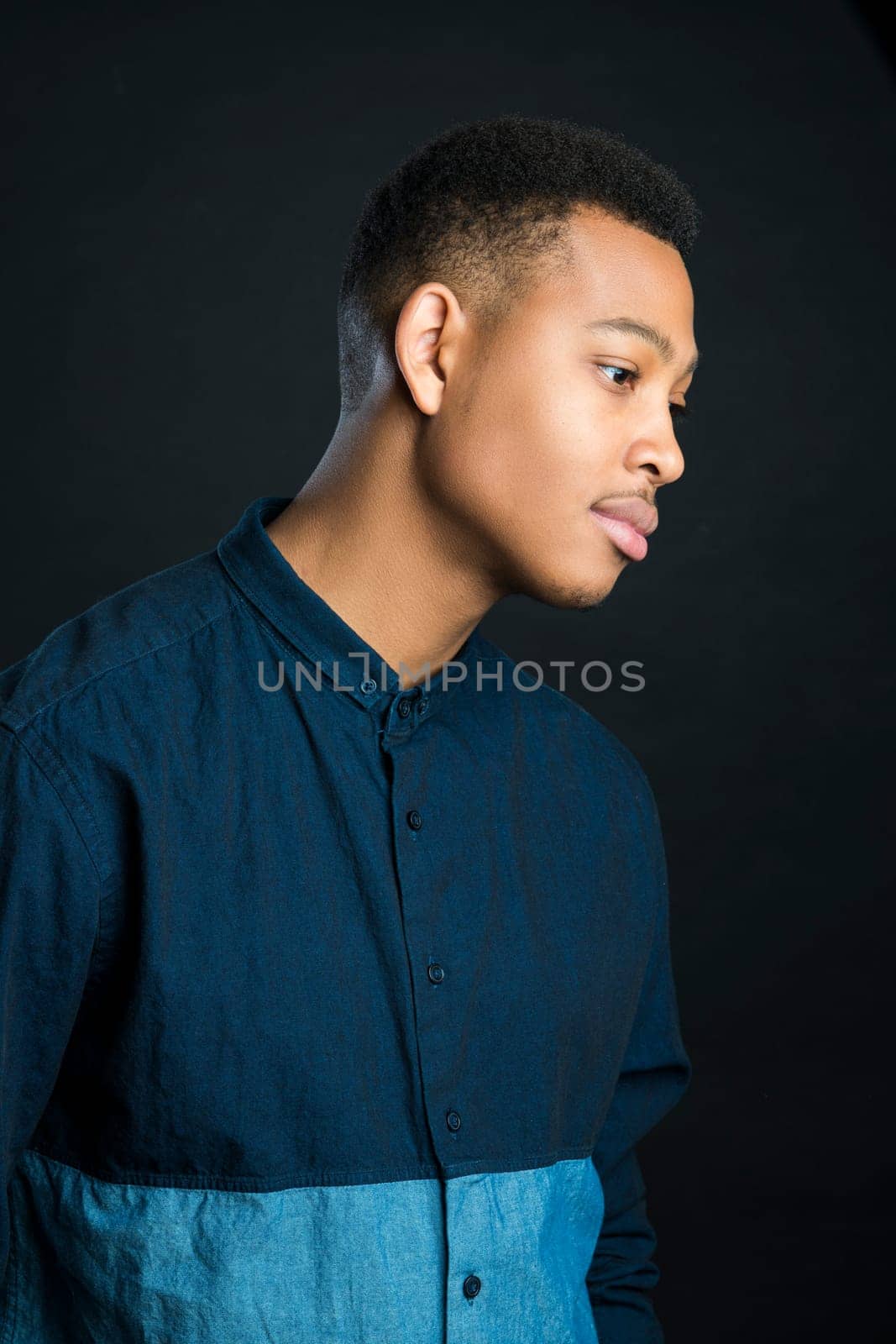 Profile portrait of handsome dark skinned male model wearing casual clothes against black background
