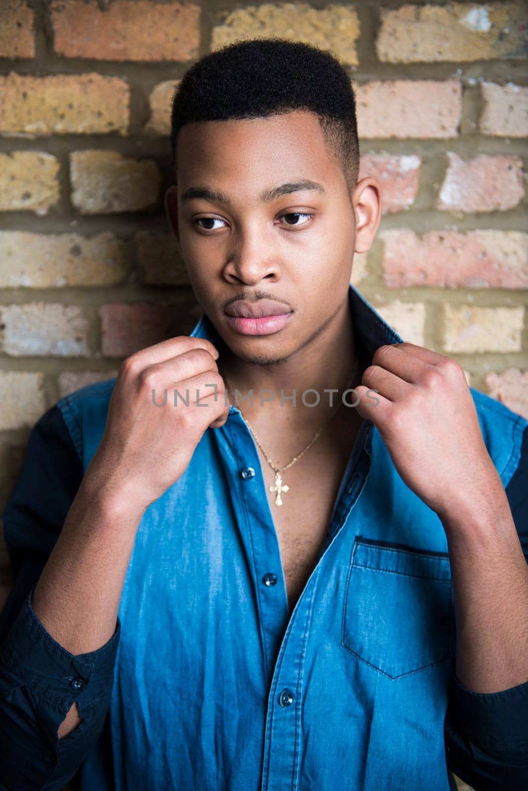 Portrait of handsome dark skinned male model wearing casual clothes against brick wall