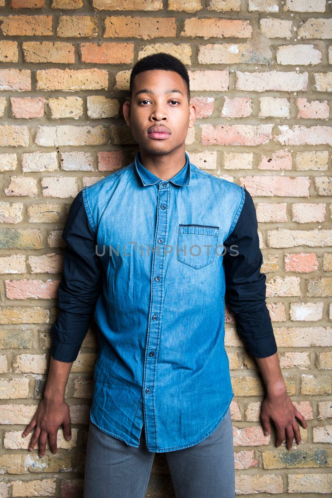 Portrait of handsome dark skinned male model wearing casual clothes against brick wall