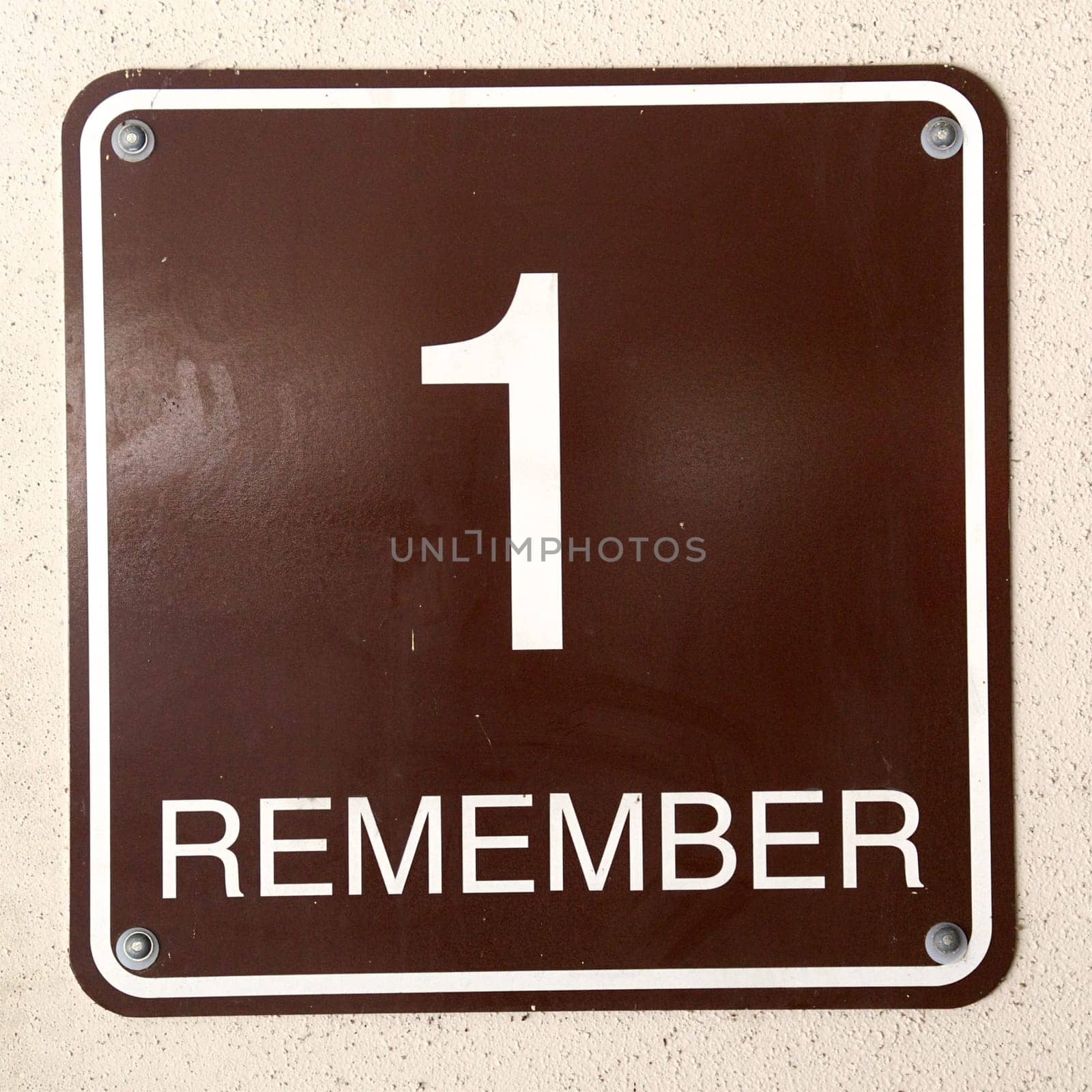 A square sign on wall that states "1 Remember"" as seen near exit of parking garage."