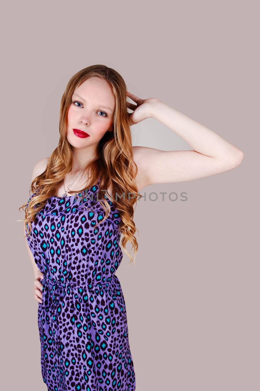 A pretty teenage girl in a blue dress with long blond hair standing.isolated for light grey background..