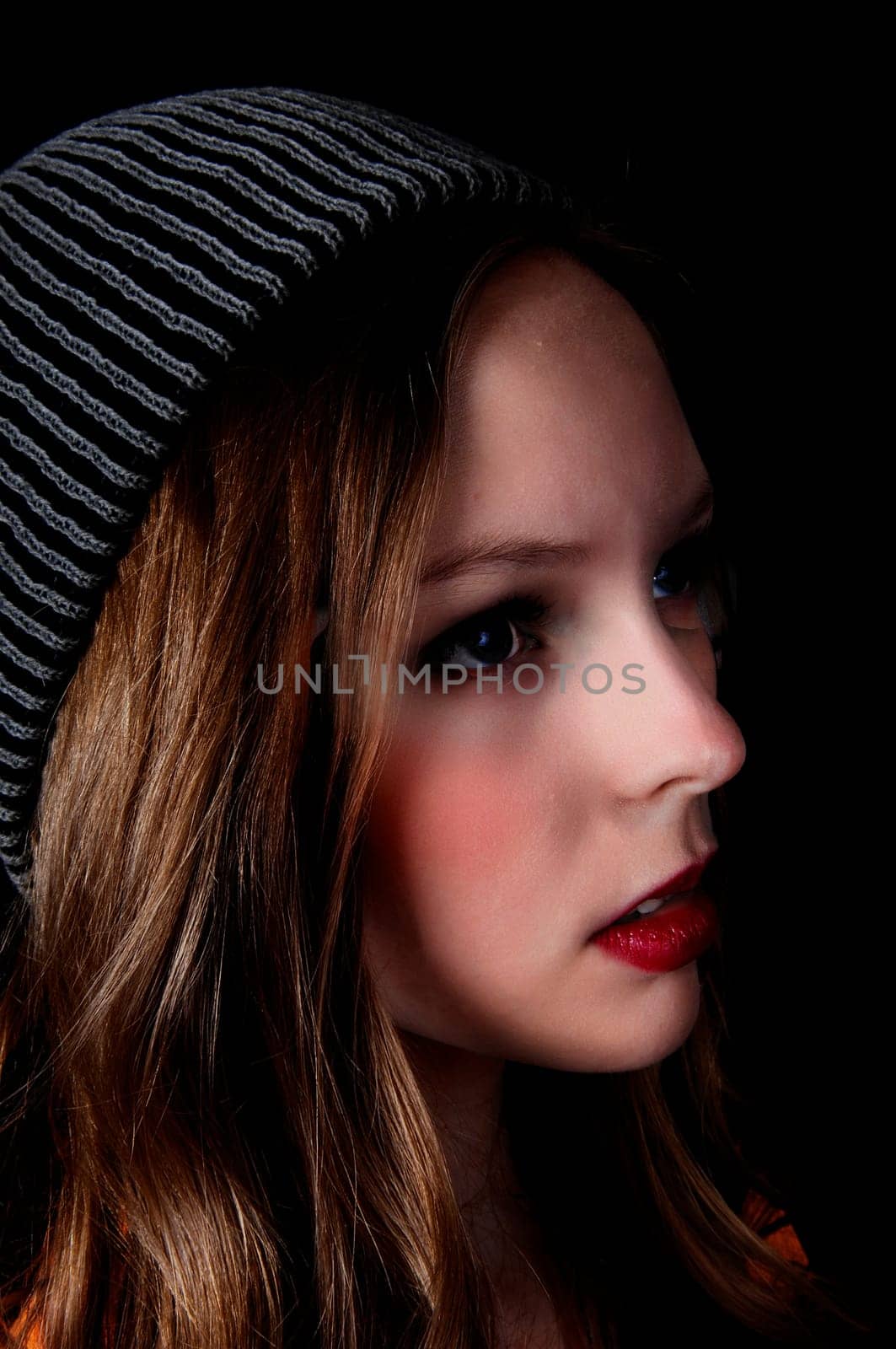 A profile portrait picture of a teenage girl wearing a knitted hat, .isolated for black background..