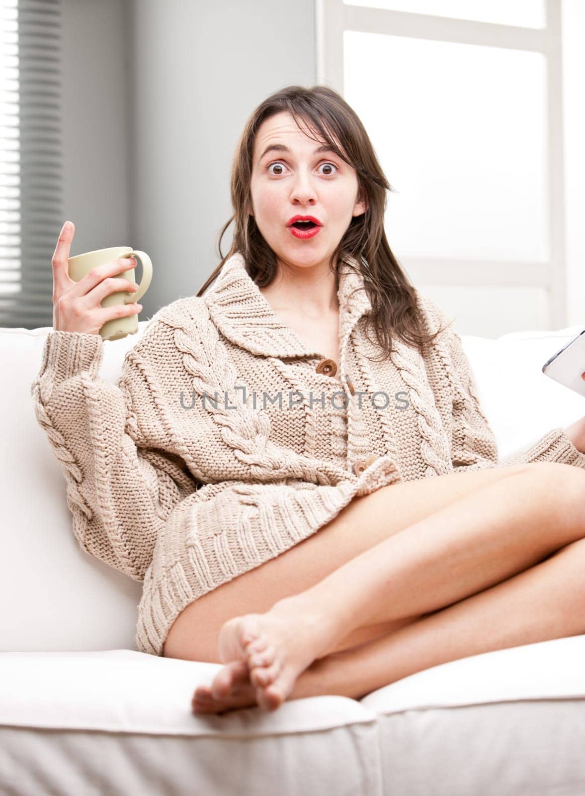 astonished girl on a sofa with a mug and a tablet