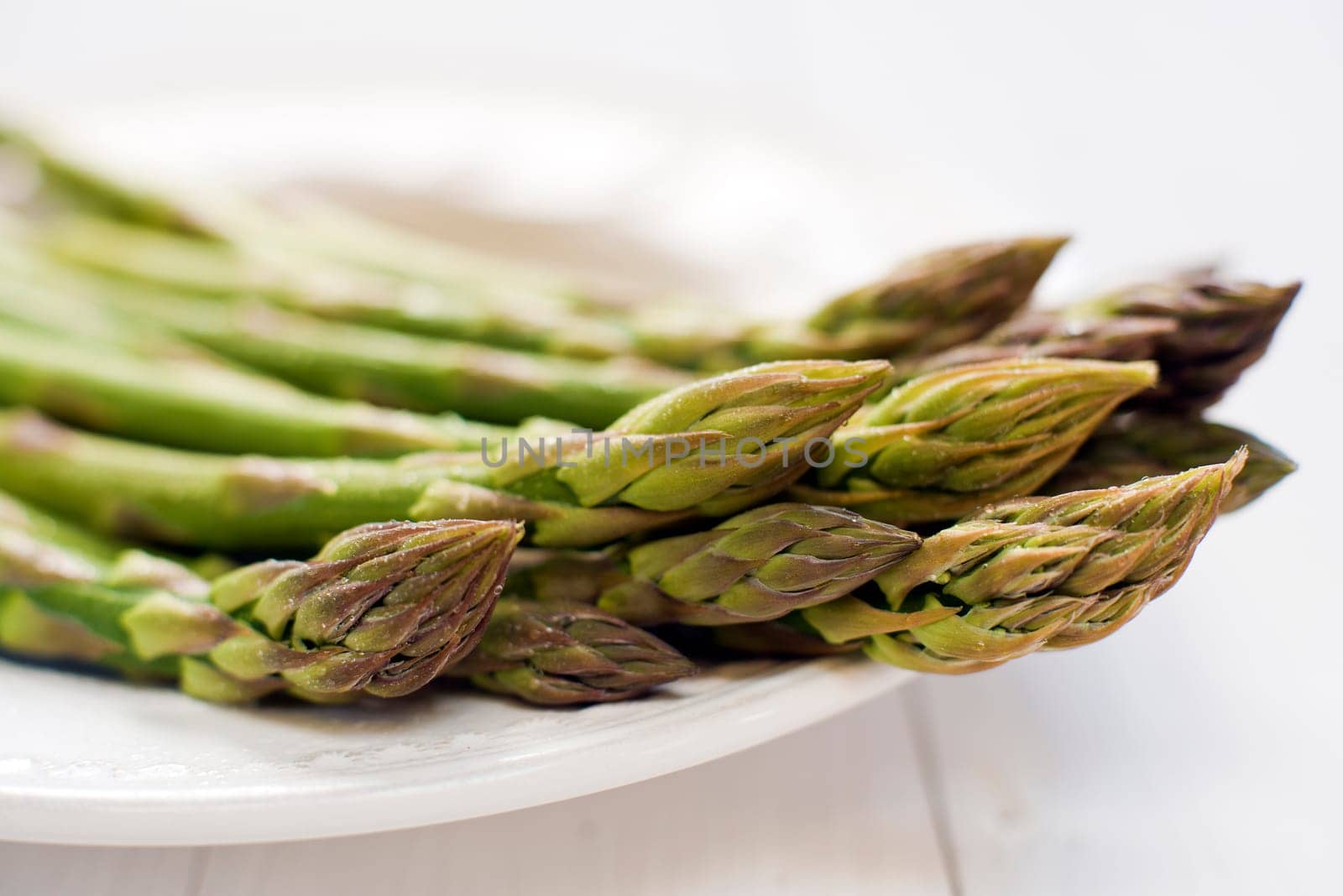 Fresh green asparagus on white plate close up