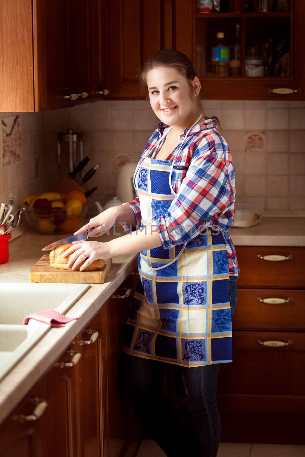 Beautiful smiling woman cutting bread on wooden cutting board