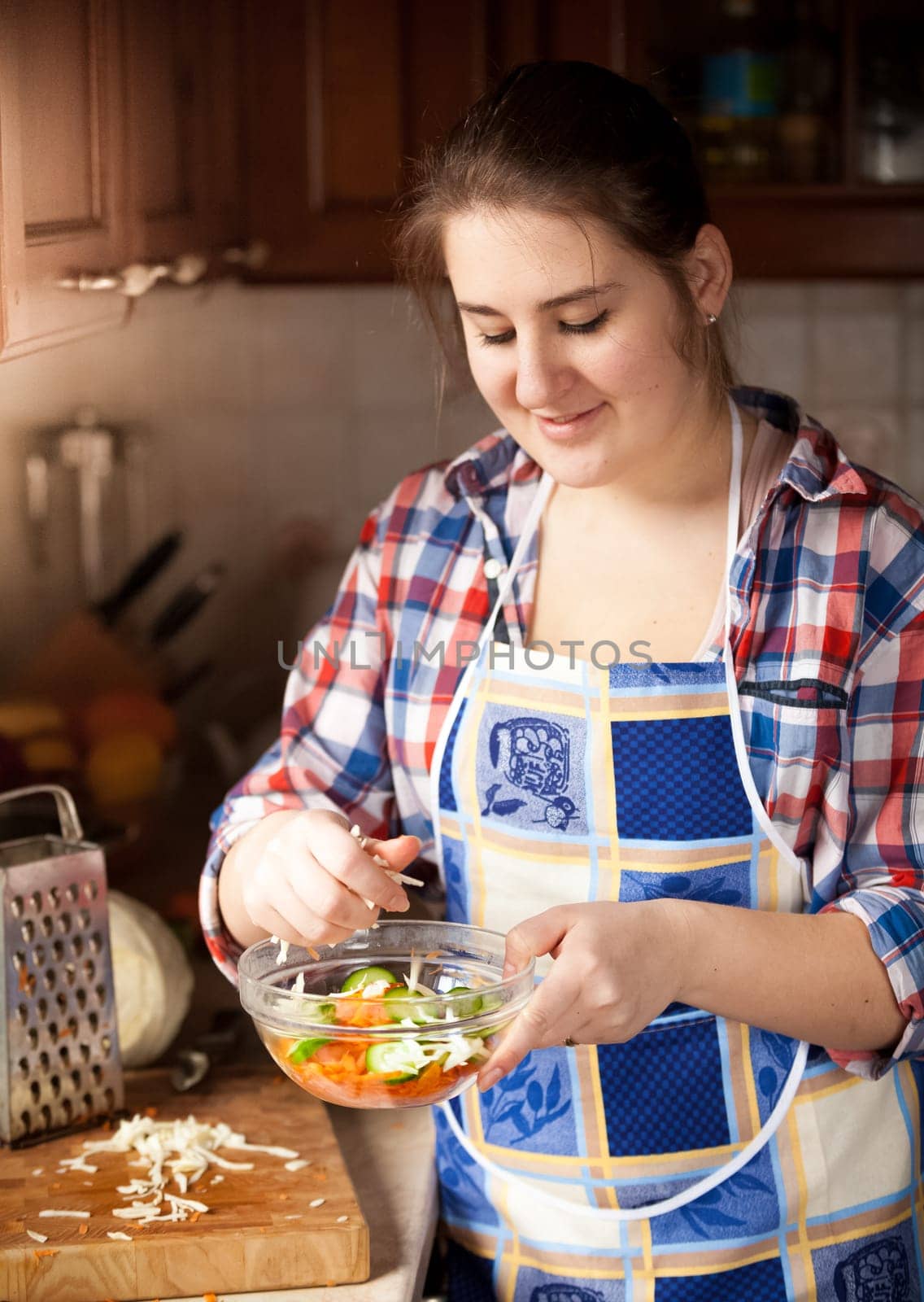 Portrait of young housewife preparing salad with cucumbers