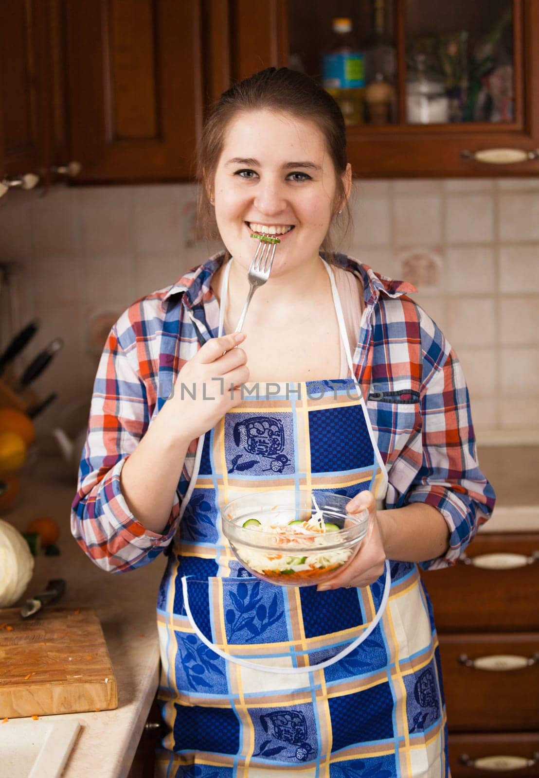 Portrait of happy housewife eating cucumbers from salad