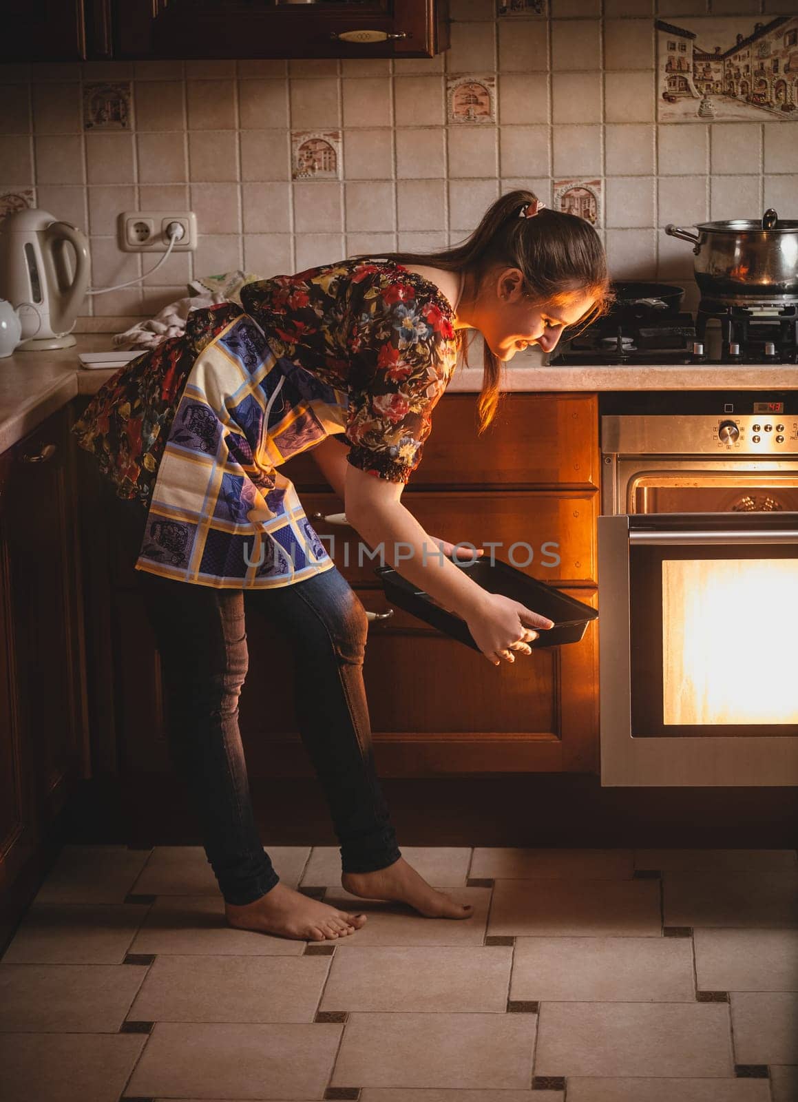 Young housewife holding cookies on pan near oven