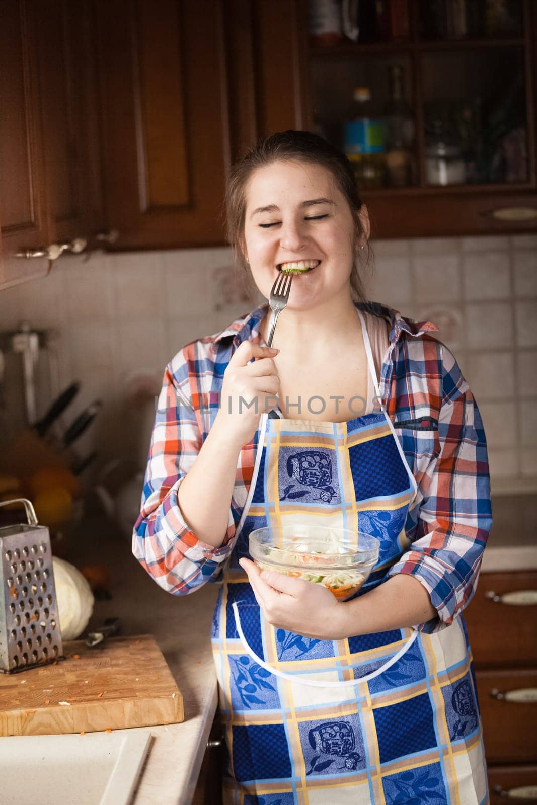 Portrait of happy housewife eating cucumbers from salad