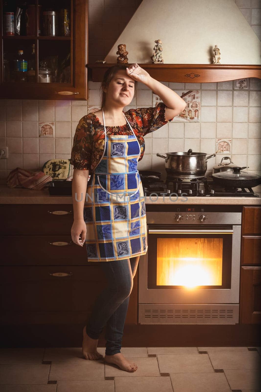 Young tired housewife standing near working oven
