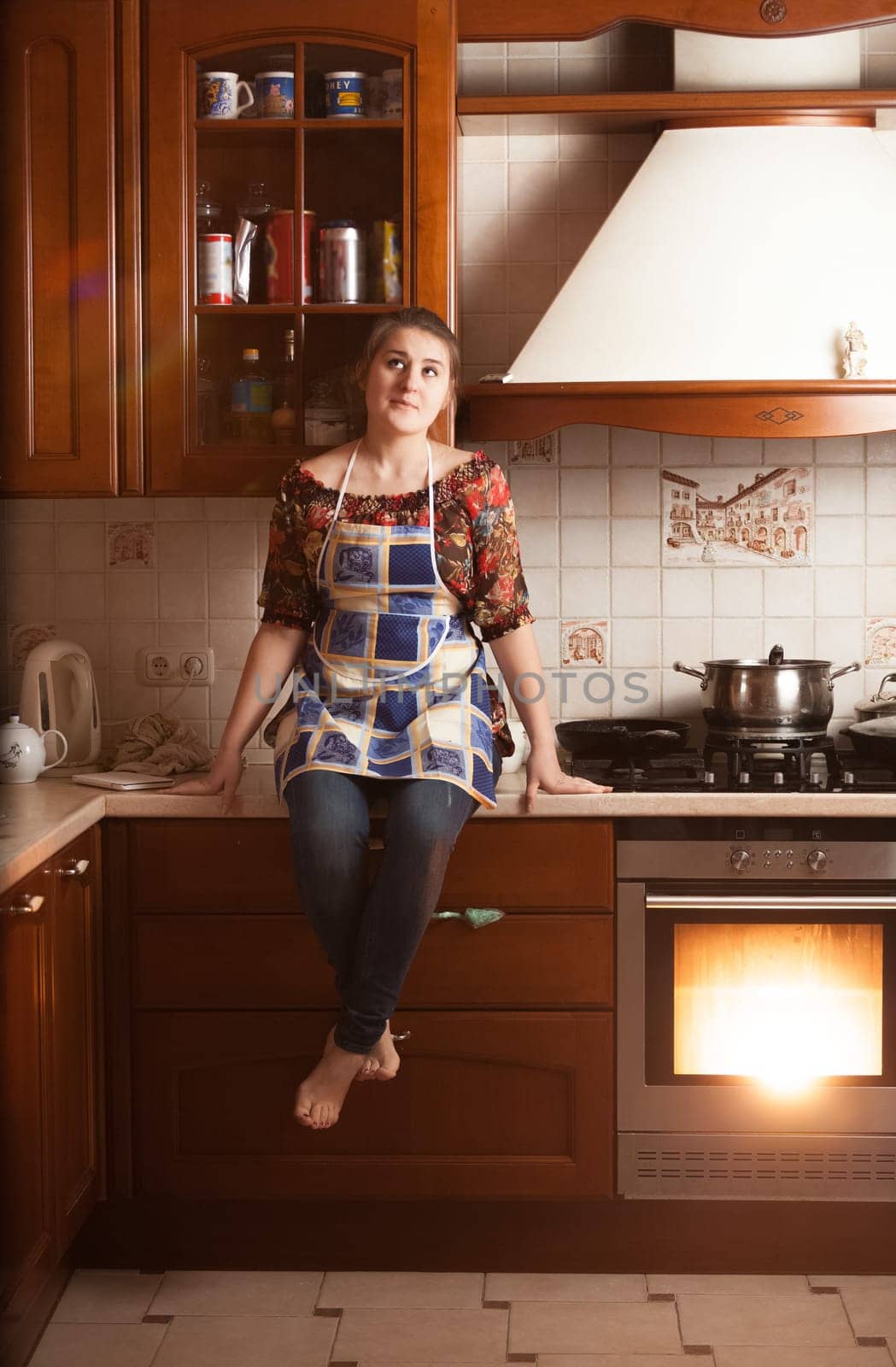 Beautiful housewife sitting on tabletop near working oven