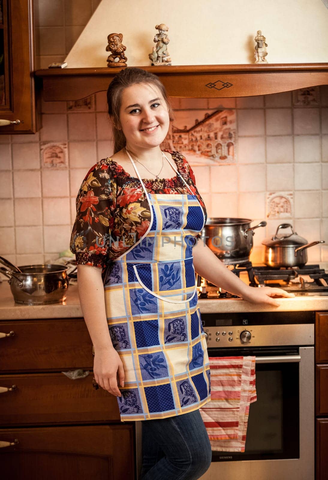 Portrait of beautiful housewife posing against gas stove with saucepans