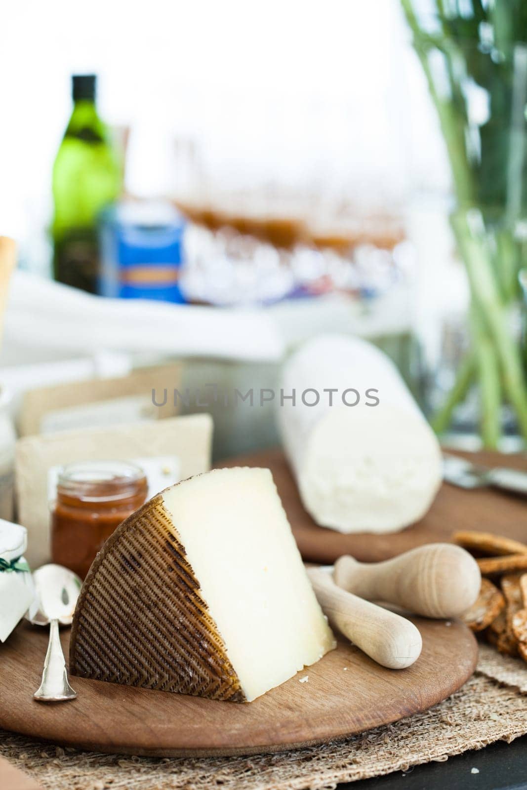 Closeup of piece of cheese and condiment in jar on wooden cutting board with cheese in background