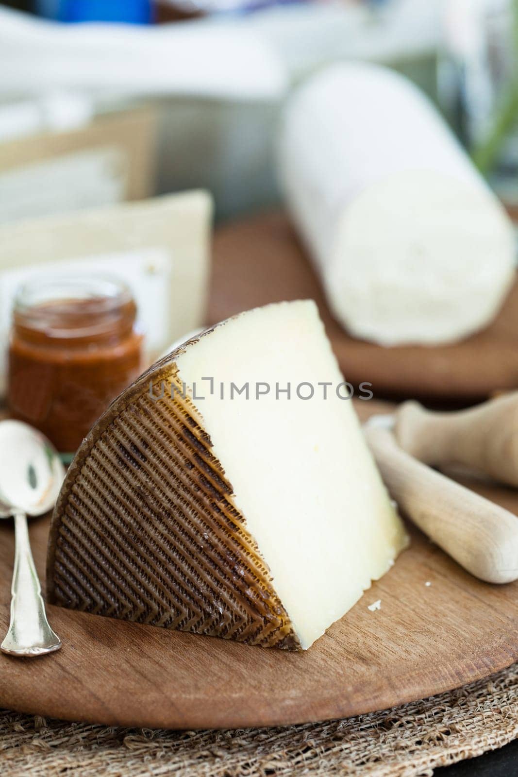 Closeup of piece of cheese and condiment in jar on wooden cutting board with cheese in background