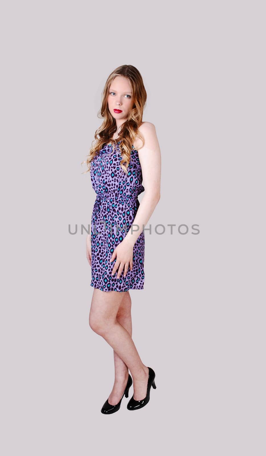 A pretty teenage girl in a blue dress with long blond hair standing.isolated for light grey background..