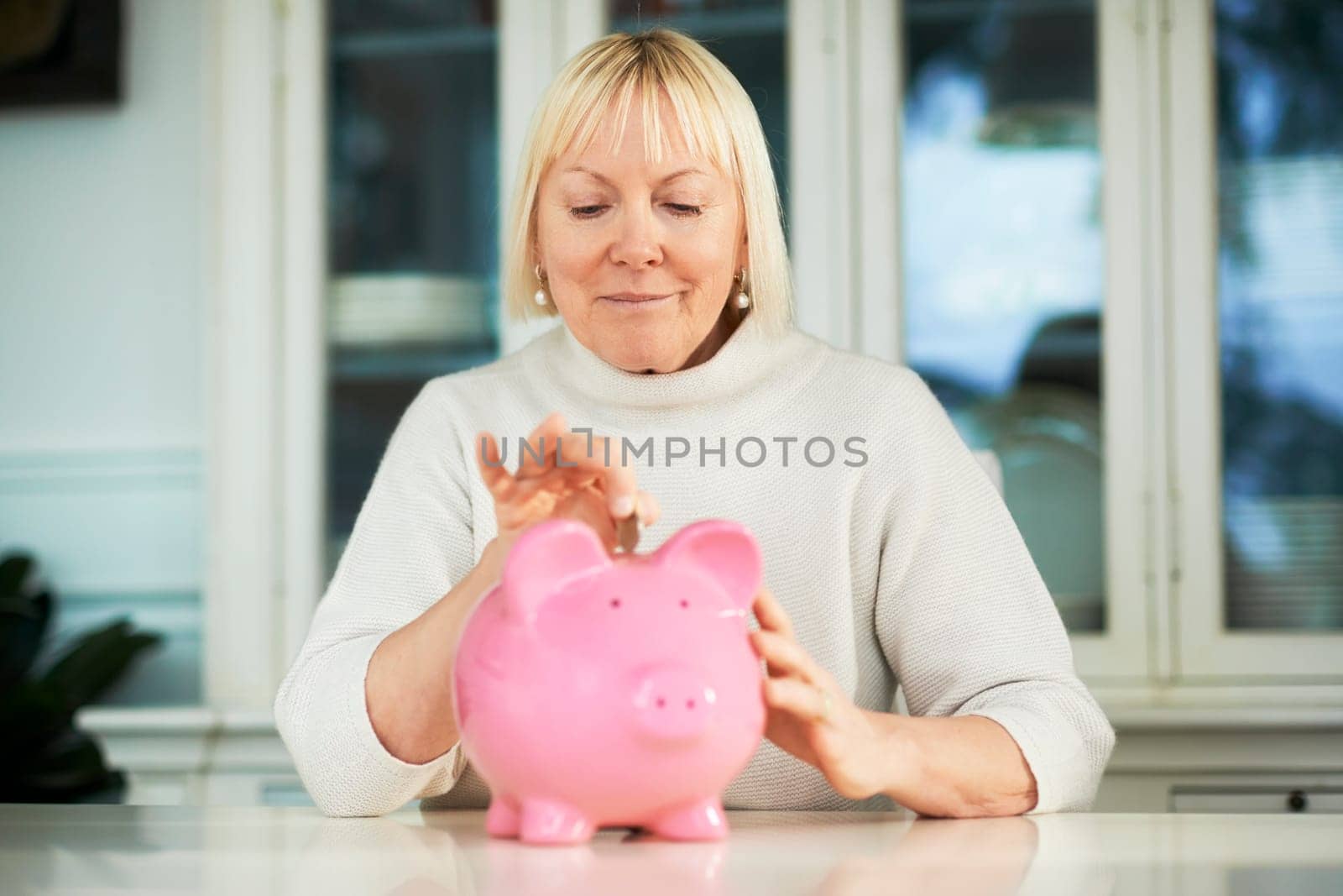 portrait of happy caucasian senior woman saving euro coin into piggybank and smiling